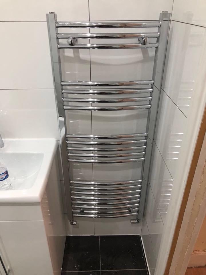 Tiled bathroom with chrome towel radiator and bath