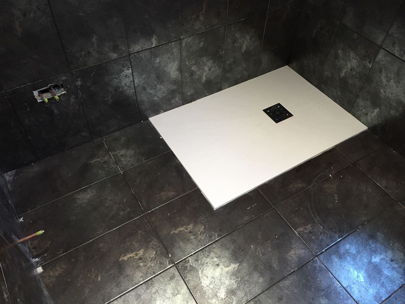 Wet room shower tray laid flush into black floor tiles