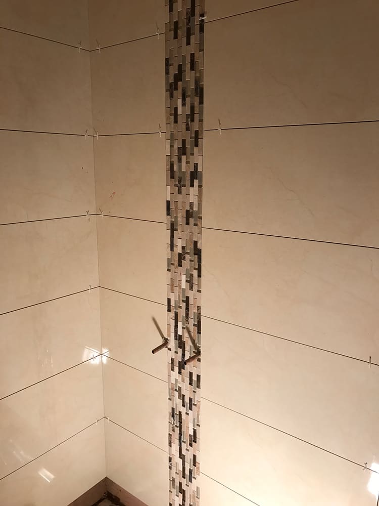Mosaic border tiles being set into a bathroom wall