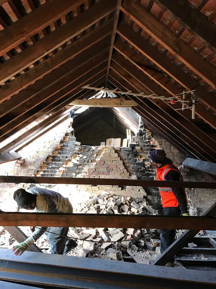 Operative working in the stripped loft between rafters