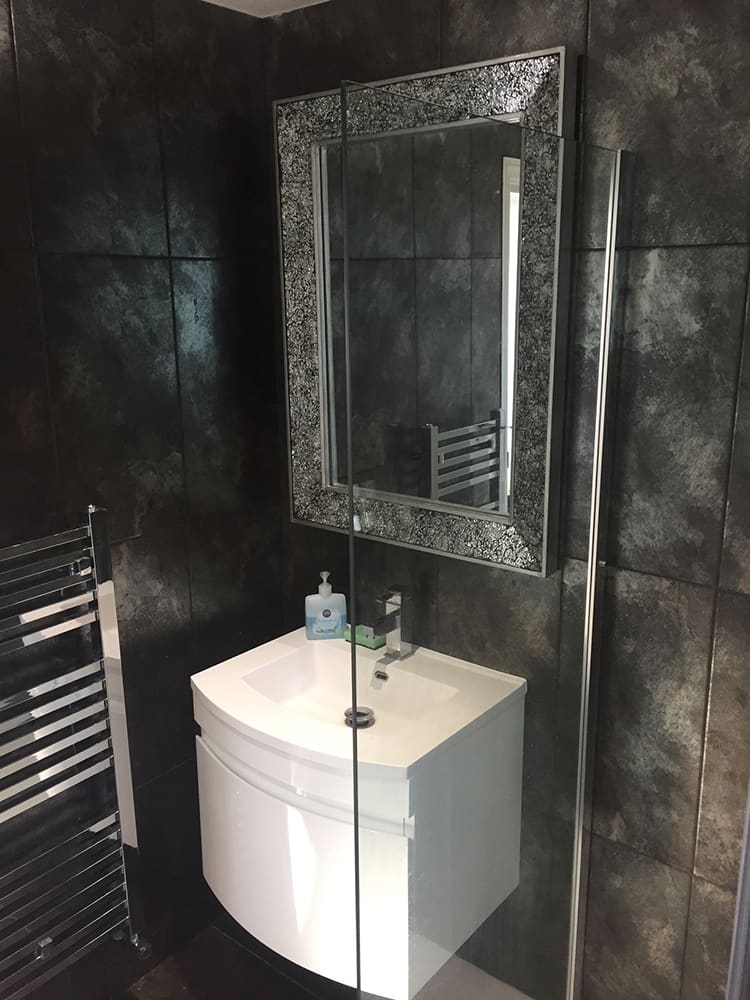 Dark stone-tiled bathroom with basin, mirror and towel rail