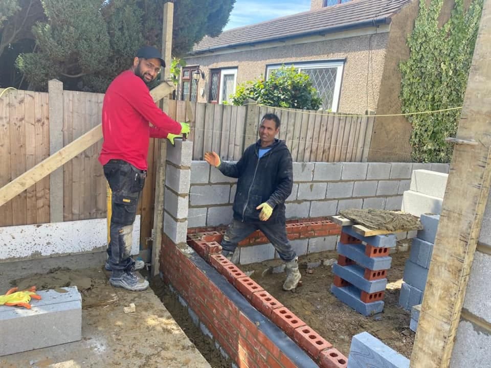 Two bricklayers building blockwork cavity walls off the new footings
