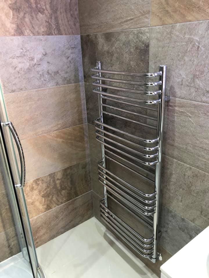 Chrome towel radiator mounted on stone-effect tiling