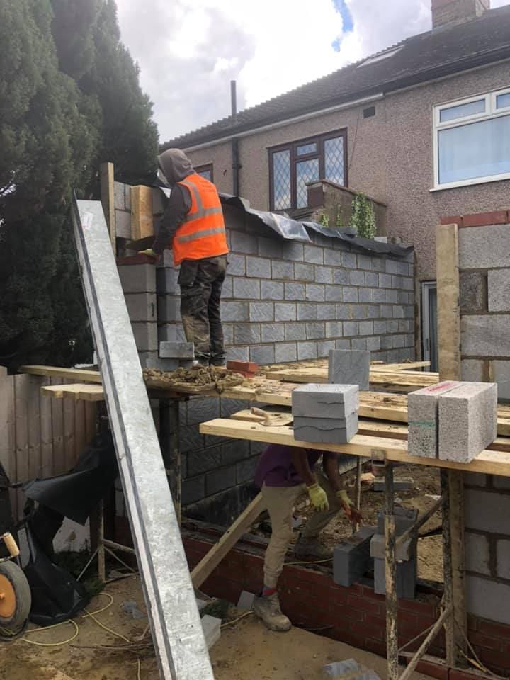 Operative laying blocks on the boundary wall with paving stacked nearby